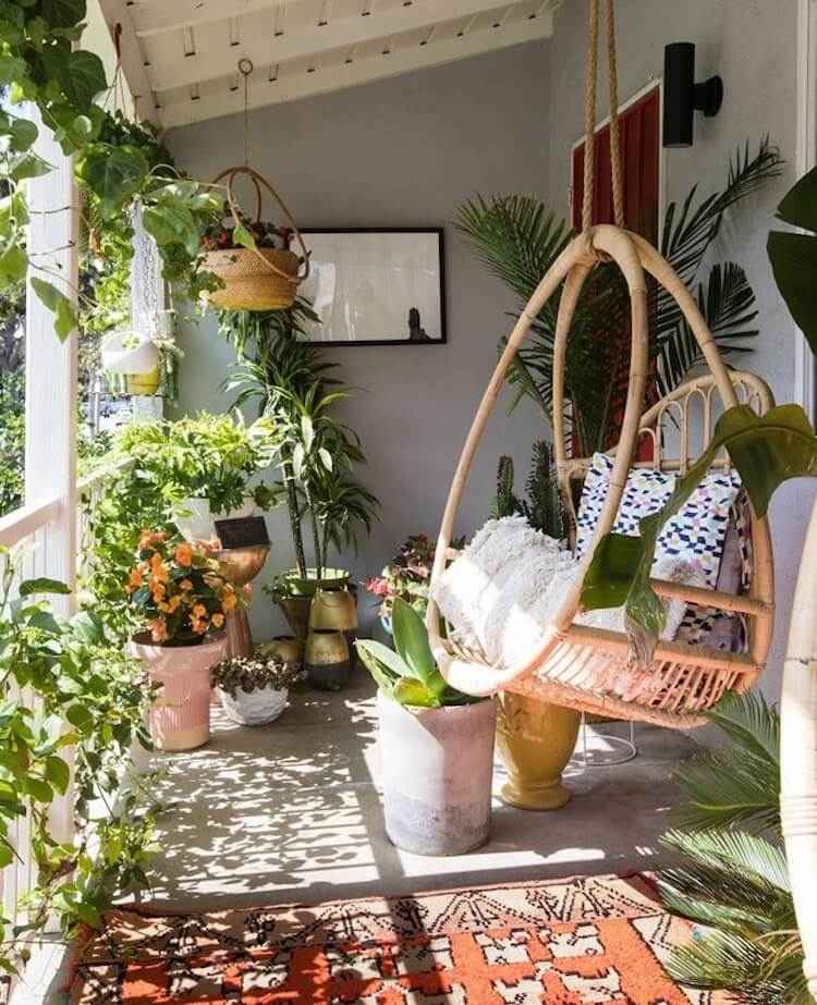 balkon w miejskiej dżungli z dużą ilością roślin i wiszącymi krzesłami